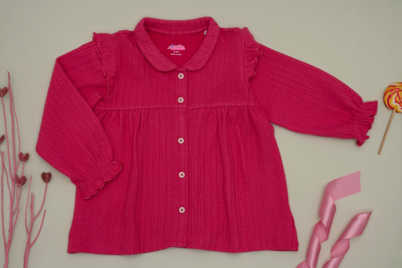 A vibrant pink long sleeve blouse with decorative elements, perfect for childrens fashion.